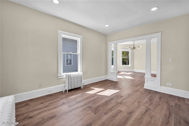 unfurnished room with radiator heating unit, a chandelier, wood finished floors, baseboards, and recessed lighting
