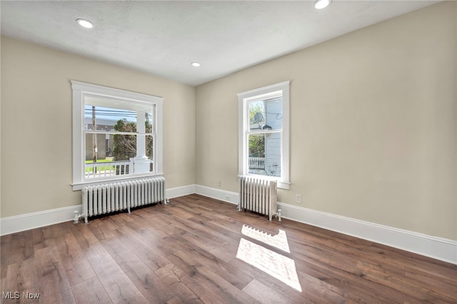 spare room featuring radiator heating unit, plenty of natural light, wood-type flooring, and recessed lighting