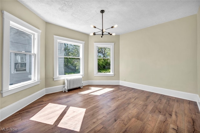 unfurnished dining area featuring radiator heating unit, a chandelier, dark wood-style floors, a textured ceiling, and baseboards