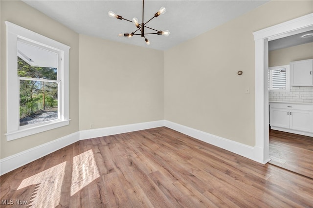 unfurnished dining area with a chandelier, light wood-style flooring, and baseboards