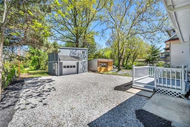 view of yard with an outdoor structure, a storage unit, a garage, a deck, and gravel driveway