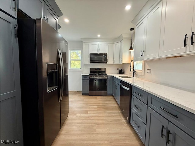 kitchen with appliances with stainless steel finishes, a sink, light wood-style floors, gray cabinets, and pendant lighting