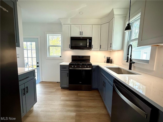 kitchen featuring dishwasher, black gas range, a sink, light wood finished floors, and decorative light fixtures
