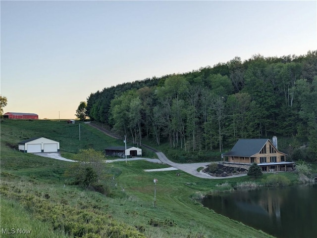 view of property's community featuring a garage, a water view, a lawn, an outbuilding, and a view of trees