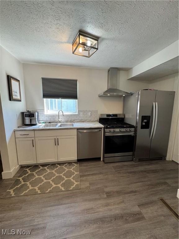5897 Kimberly Dr, Bedford Heights, OH 44146 - kitchen with appliances with stainless steel finishes, wall chimney exhaust hood, dark wood-style floors, white cabinets, and backsplash