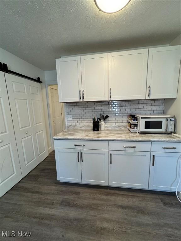 5897 Kimberly Dr, Bedford Heights, OH 44146 - kitchen with white microwave, dark wood-type flooring, white cabinetry, light countertops, and tasteful backsplash