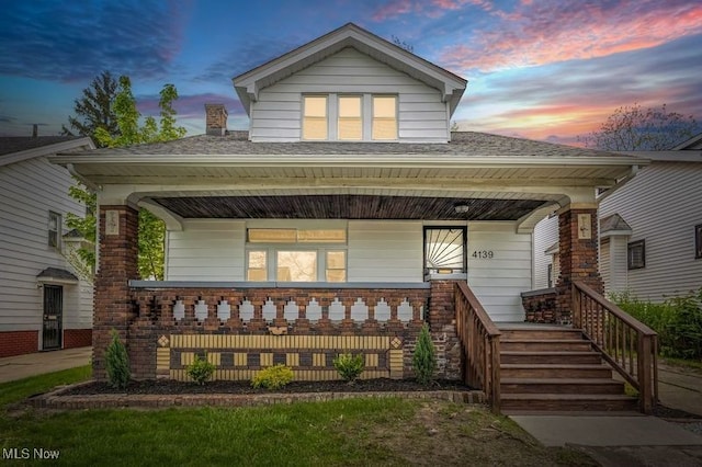 back of property at dusk with covered porch and brick siding