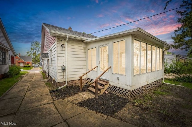 back of house at dusk with entry steps and a sunroom