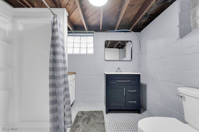 full bathroom featuring toilet, vanity, concrete block wall, tile patterned floors, and curtained shower