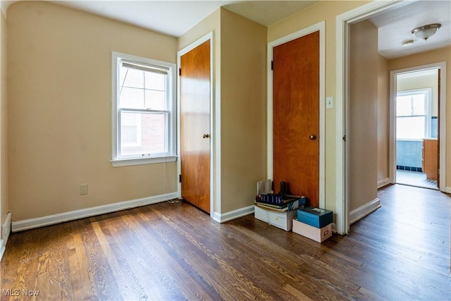 unfurnished bedroom featuring dark wood-style floors, multiple windows, and baseboards