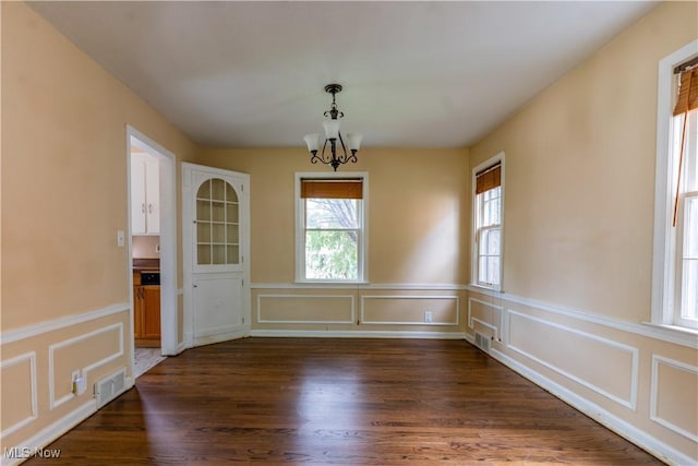 unfurnished dining area featuring a chandelier, healthy amount of natural light, dark wood-style floors, a decorative wall, and a wainscoted wall
