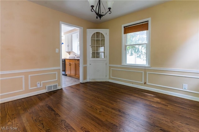 unfurnished dining area featuring a chandelier, dark wood-style flooring, a decorative wall, a wainscoted wall, and a sink