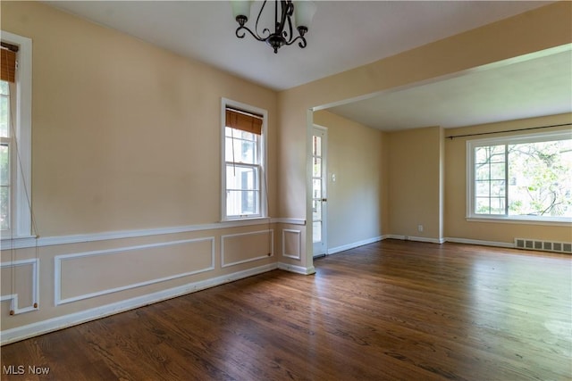 unfurnished room with wood finished floors, a chandelier, a wainscoted wall, and baseboards