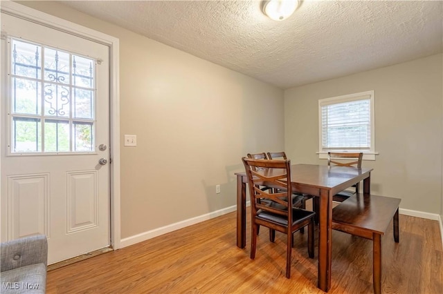 dining area with light wood-style flooring, baseboards, and a textured ceiling