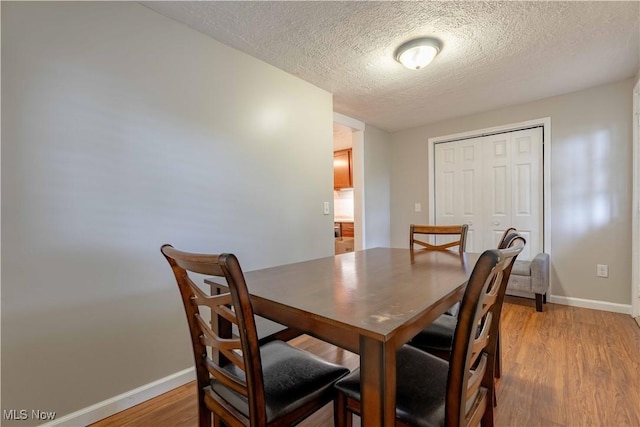dining room featuring baseboards, light wood-style floors, and a textured ceiling