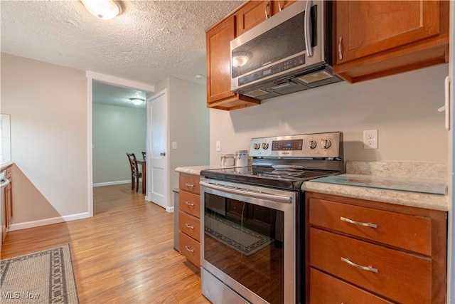 kitchen with stainless steel appliances, brown cabinets, light wood-style floors, light countertops, and a textured ceiling