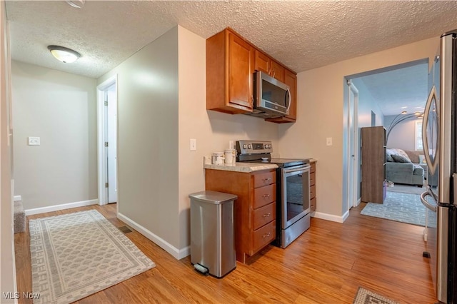 kitchen featuring appliances with stainless steel finishes, brown cabinets, a textured ceiling, light wood finished floors, and light countertops