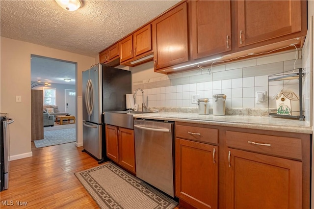 kitchen featuring appliances with stainless steel finishes, brown cabinets, light wood-style flooring, decorative backsplash, and a textured ceiling