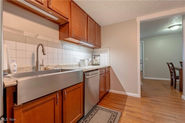 kitchen with dishwasher, a sink, brown cabinets, light wood finished floors, and tasteful backsplash