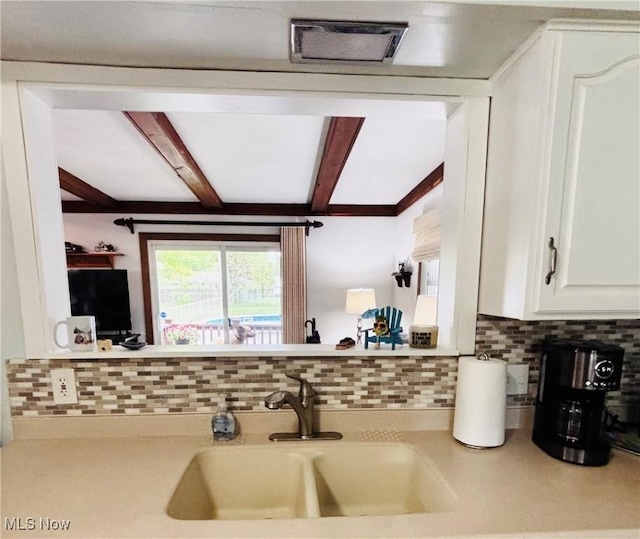 kitchen with a sink, decorative backsplash, beam ceiling, white cabinetry, and light countertops