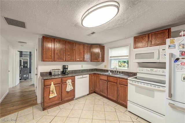 kitchen with white appliances, a sink, brown cabinets, dark countertops, and a textured ceiling