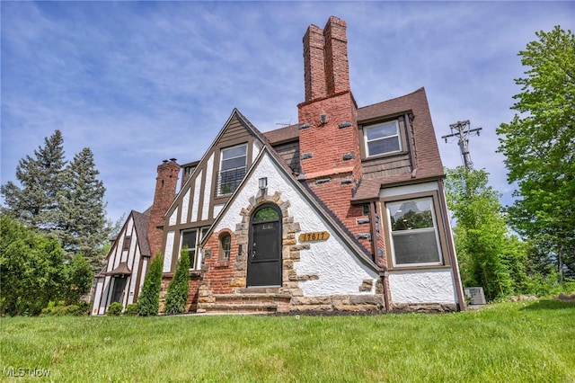 17617 Lomond Blvd, Shaker Heights, OH 44120 - tudor home with a chimney, stone siding, a front yard, entry steps, and roof with shingles