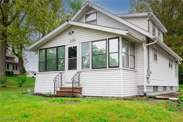 view of front facade with entry steps, a sunroom, and a front yard