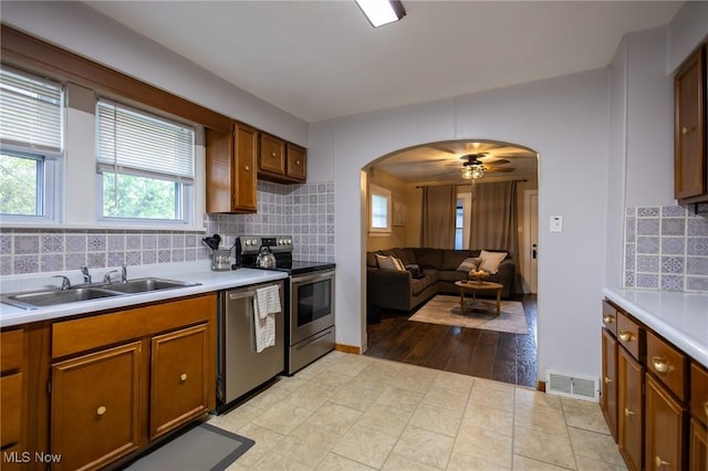kitchen with appliances with stainless steel finishes, a sink, arched walkways, light countertops, and brown cabinets