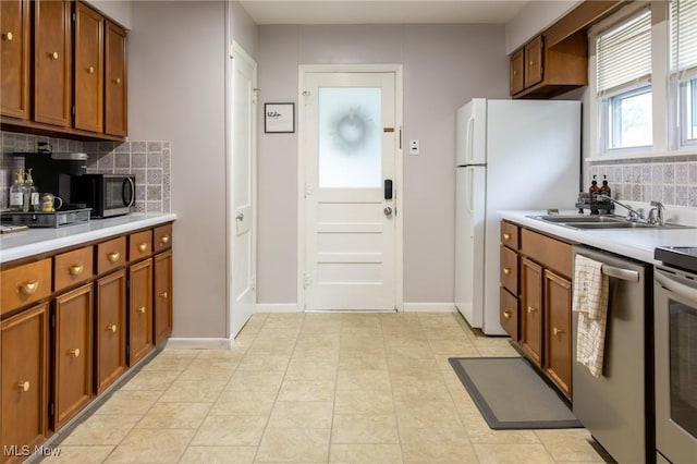 kitchen with stainless steel appliances, a sink, decorative backsplash, and brown cabinets