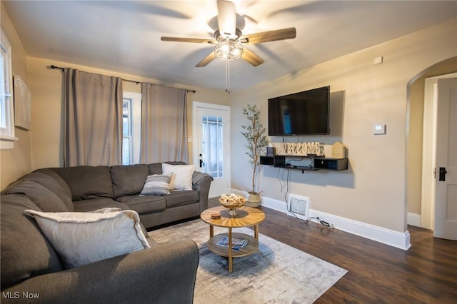 living area featuring ceiling fan, arched walkways, wood finished floors, baseboards, and plenty of natural light
