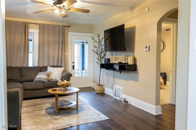 living area featuring arched walkways, ceiling fan, dark wood-type flooring, and baseboards