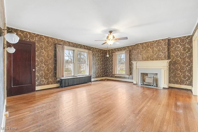 245 Merriman Rd, Akron, OH 44303 - unfurnished living room with radiator, wood-type flooring, wallpapered walls, a ceiling fan, and a fireplace with flush hearth