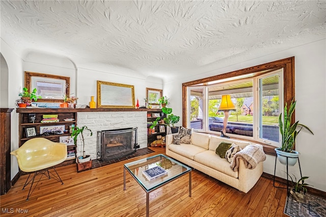 living area featuring a stone fireplace, hardwood / wood-style flooring, a textured ceiling, and arched walkways