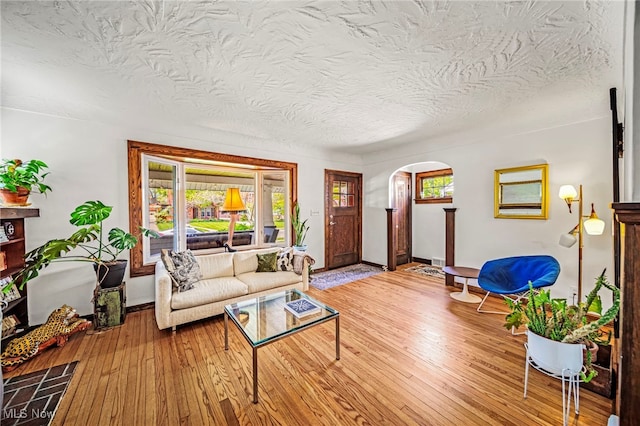 living area with arched walkways, plenty of natural light, a textured ceiling, hardwood / wood-style floors, and baseboards