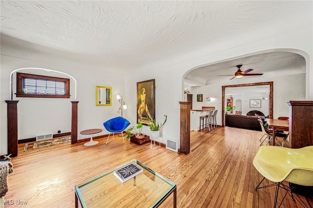 living area with arched walkways, ceiling fan, wood finished floors, a textured ceiling, and baseboards