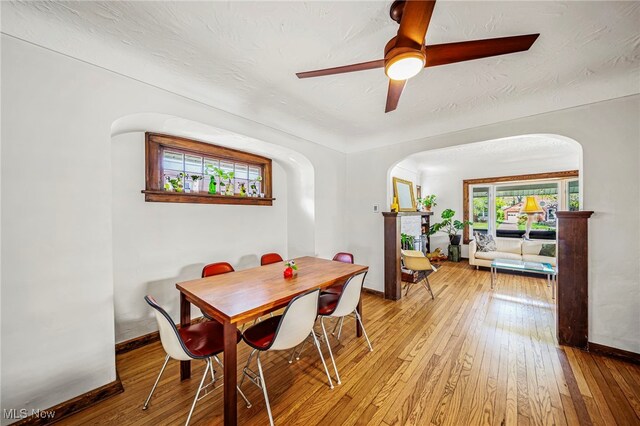 dining space featuring arched walkways, hardwood / wood-style floors, baseboards, and ceiling fan