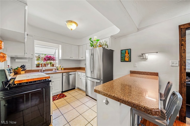 kitchen with stainless steel appliances, a sink, a peninsula, white cabinetry, and light tile patterned floors