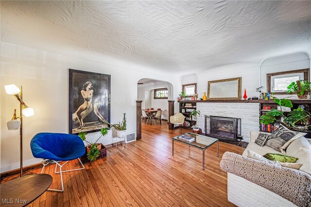 living room with arched walkways, baseboards, wood-type flooring, a textured ceiling, and a fireplace with flush hearth
