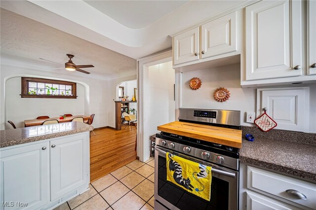 kitchen featuring stainless steel range oven, arched walkways, light tile patterned flooring, white cabinetry, and butcher block countertops