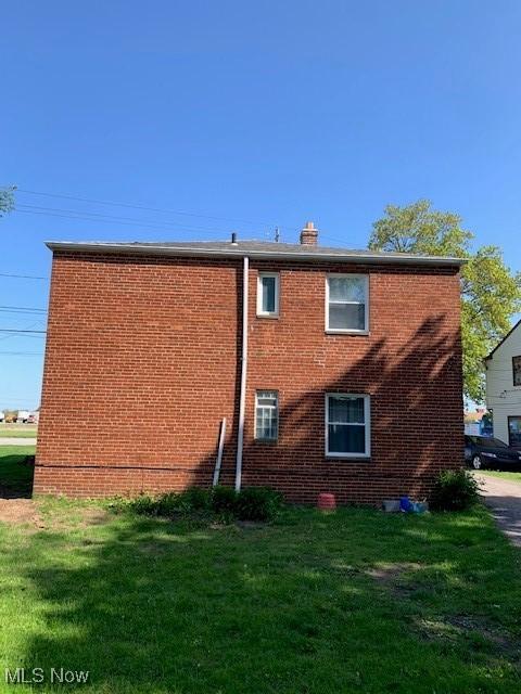 back of property featuring brick siding, a yard, and a chimney