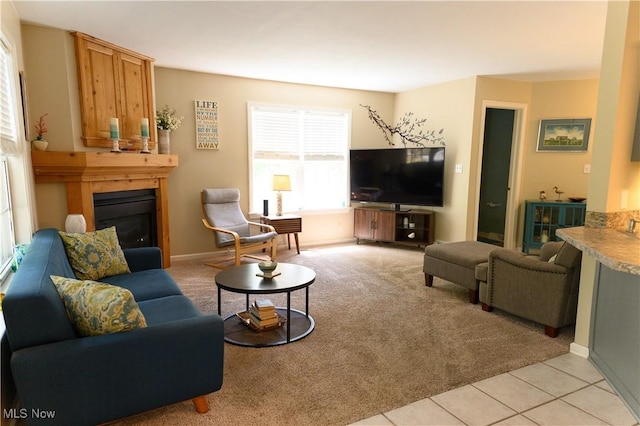 living area with light colored carpet, a glass covered fireplace, light tile patterned floors, and baseboards