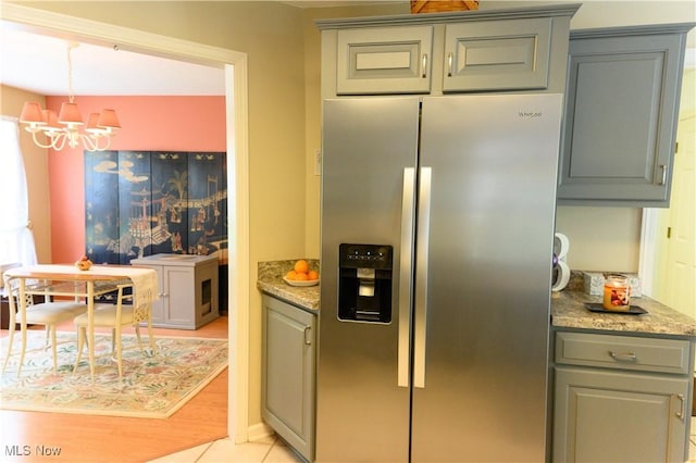 kitchen featuring stainless steel fridge, a chandelier, gray cabinets, and light stone countertops