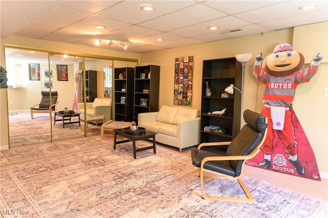 carpeted living area with a paneled ceiling and baseboards