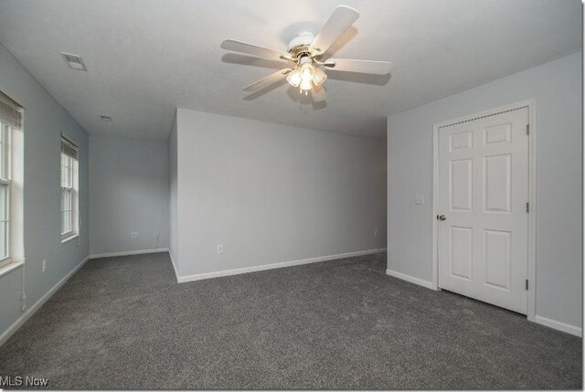 empty room with dark colored carpet, baseboards, and ceiling fan
