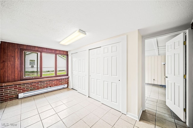 unfurnished bedroom featuring a baseboard radiator, a textured ceiling, light tile patterned floors, two closets, and brick wall