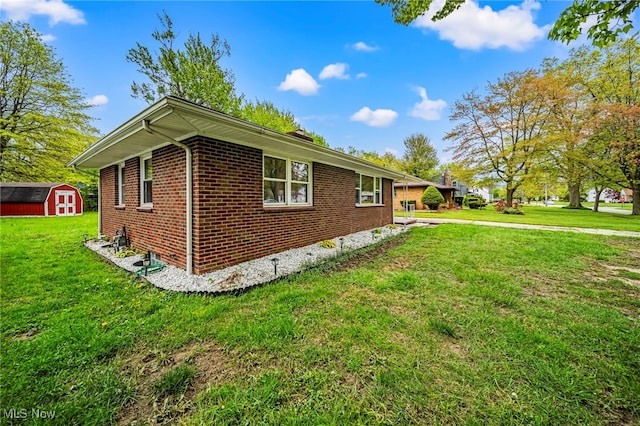view of side of home with a storage unit, brick siding, a lawn, and an outbuilding