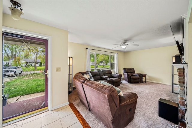 living area featuring light colored carpet, a ceiling fan, light tile patterned flooring, and baseboards