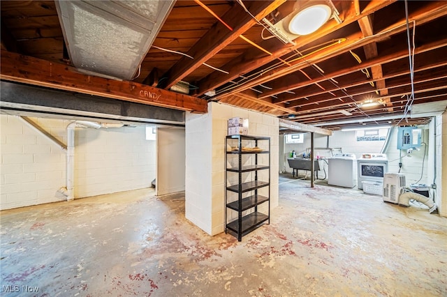 basement with washing machine and clothes dryer, electric panel, and concrete block wall