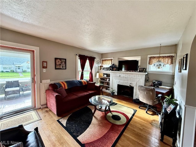 living area featuring a textured ceiling, light wood-type flooring, and a brick fireplace
