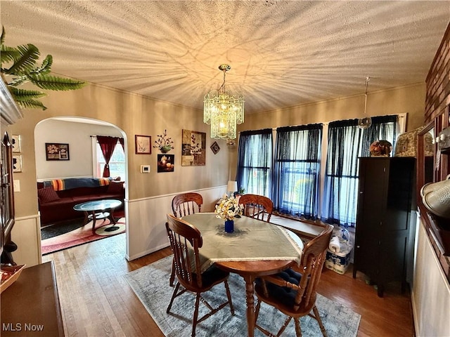 dining room featuring arched walkways, wood finished floors, a chandelier, and a wainscoted wall